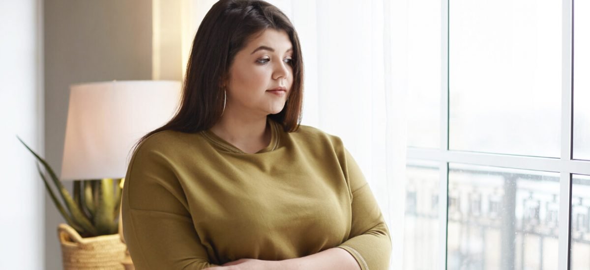 people-lifestyle-and-body-positivity-concept-beautiful-young-brunette-female-with-extra-pounds-standing-by-window-at-home-crossing-arms-on-her-chest-having-thoughtful-pensive-look-pondering