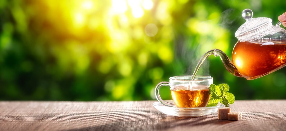 Pouring,Black,Tea,Into,Glass,Cup,On,Wooden,Table
