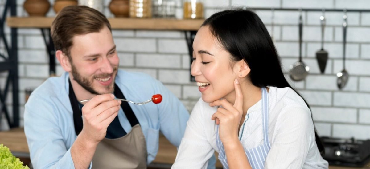 smiling-couple-feeding-healthy-salad-in-kitchen-wearing-apron